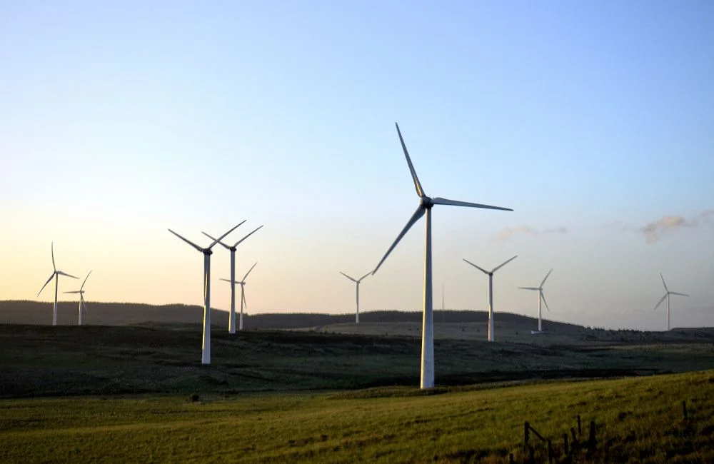 Wind turbines on green hills during sunset generating renewable wind energy.