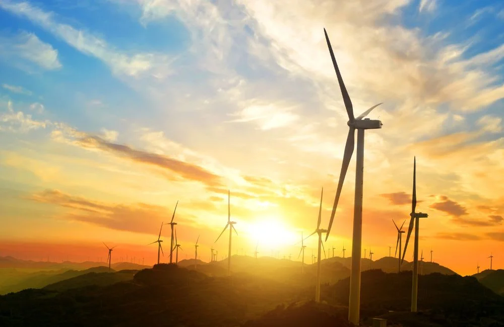 Wind turbines generating renewable energy during sunset over a hilly landscape