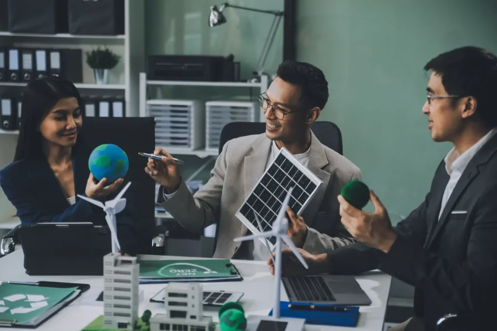 Team discussing renewable energy solutions with solar panel and wind turbine models in office