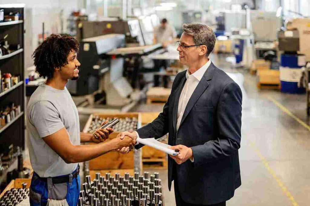 Business handshake in casting manufacturing unit between supplier and client discussing industrial components