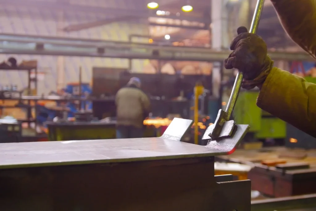 Industrial metal casting finishing process with worker shaping heated steel component in factory