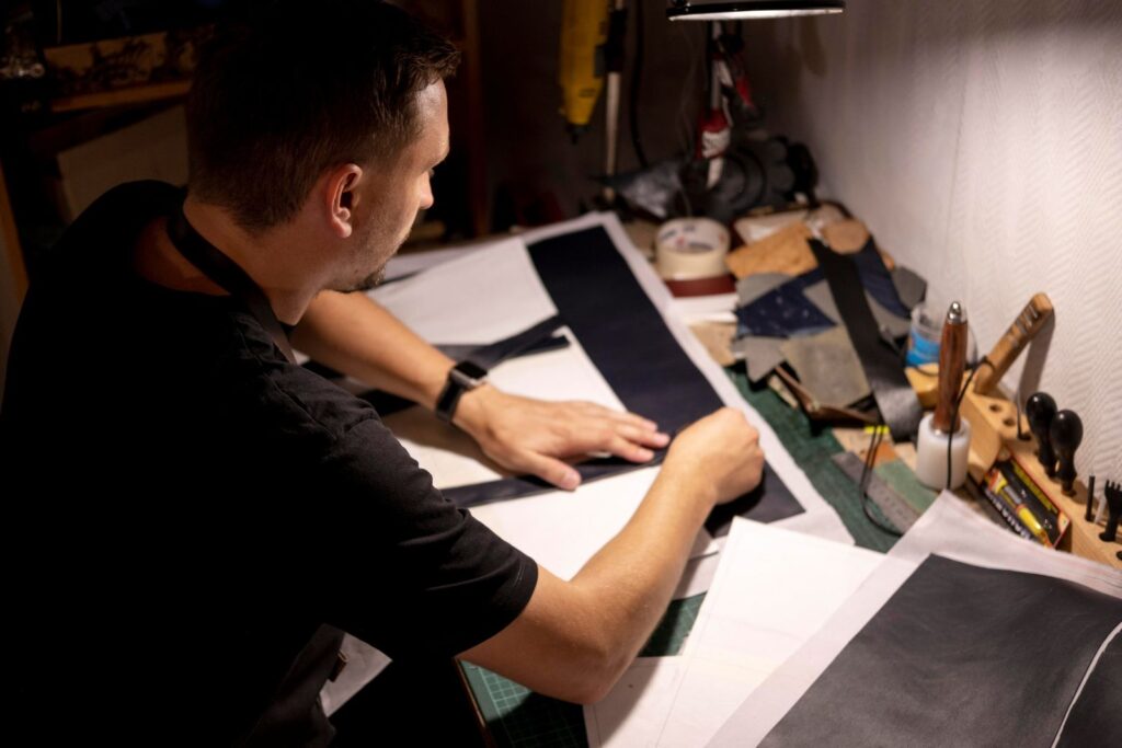 A person cutting leather or fabric pieces for crafting in a dimly lit workspace.