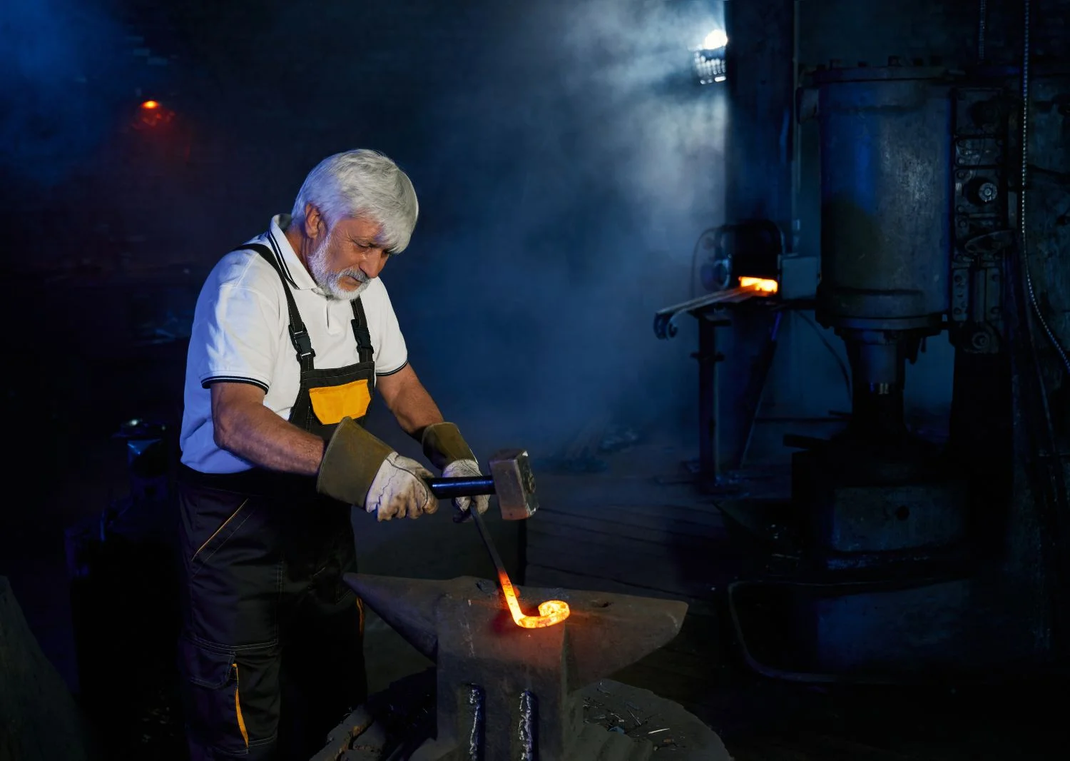 Blacksmith forging metal with a hammer on an anvil in a dark workshop.